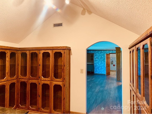 hall with a textured ceiling, dark hardwood / wood-style floors, and vaulted ceiling