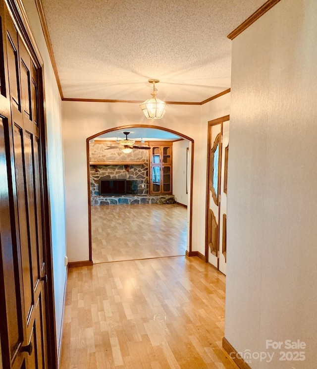 hall with arched walkways, light wood-style flooring, ornamental molding, a textured ceiling, and baseboards