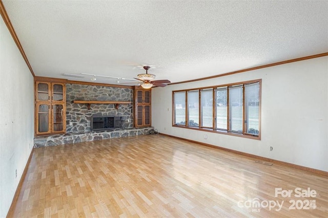 unfurnished living room featuring a textured ceiling, a stone fireplace, wood finished floors, and crown molding