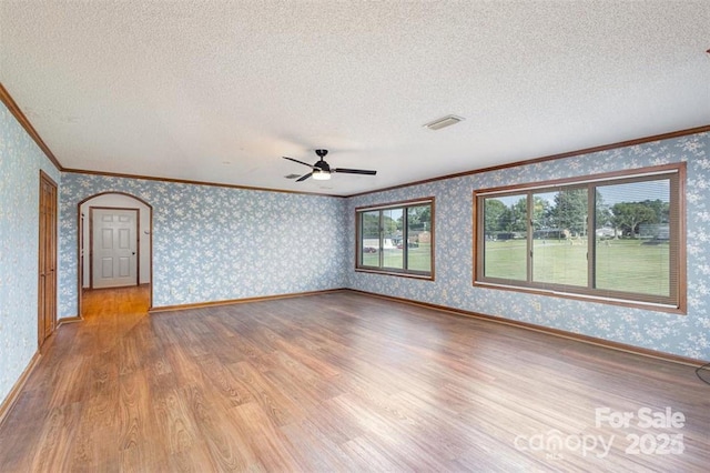 unfurnished room featuring a textured ceiling, light wood finished floors, arched walkways, and wallpapered walls