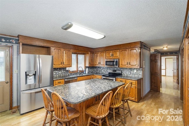 kitchen with light wood-style flooring, stainless steel appliances, a sink, brown cabinets, and dark countertops