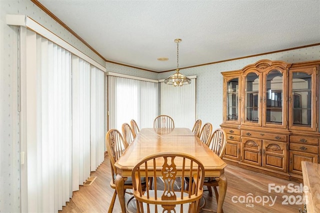 dining space featuring crown molding, light wood-style floors, a textured ceiling, and wallpapered walls