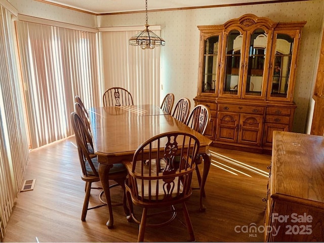 dining area with light wood-type flooring, visible vents, and wallpapered walls