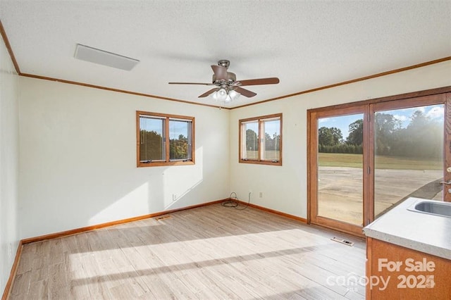 empty room with light wood finished floors, visible vents, ornamental molding, a textured ceiling, and baseboards