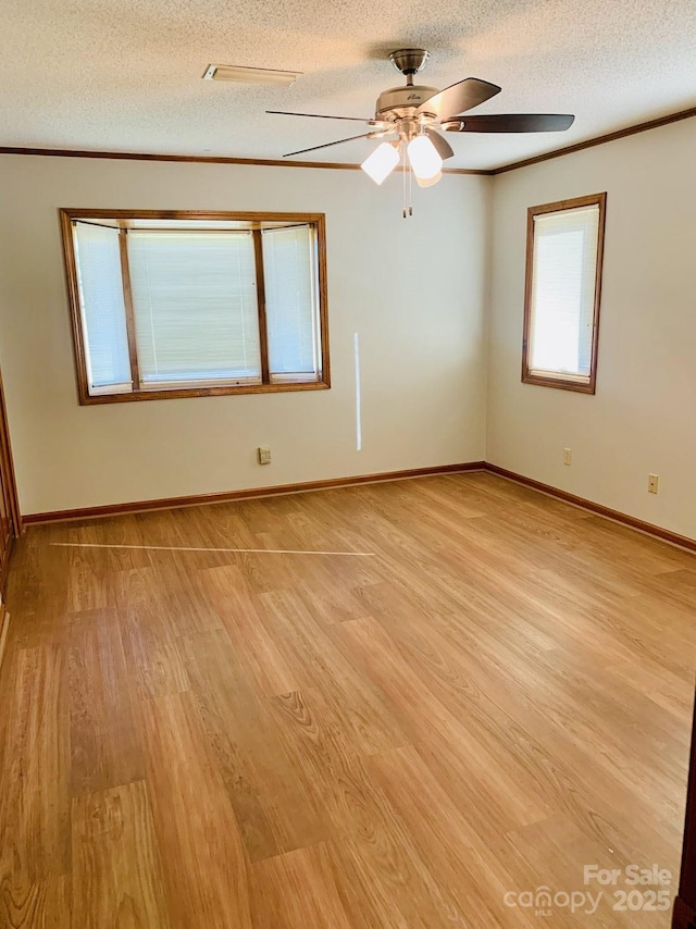 unfurnished room featuring light wood-style floors, ornamental molding, a textured ceiling, and baseboards