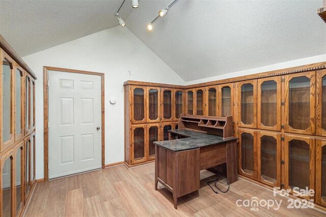 wine cellar featuring baseboards, vaulted ceiling, a textured ceiling, and light wood finished floors