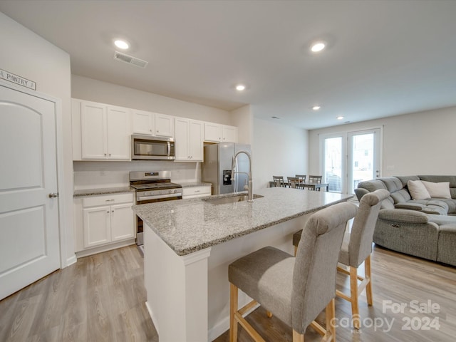 kitchen featuring a center island with sink, sink, light stone countertops, light hardwood / wood-style floors, and stainless steel appliances