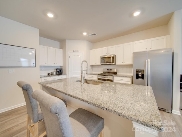 kitchen with light stone counters, stainless steel appliances, white cabinetry, and sink