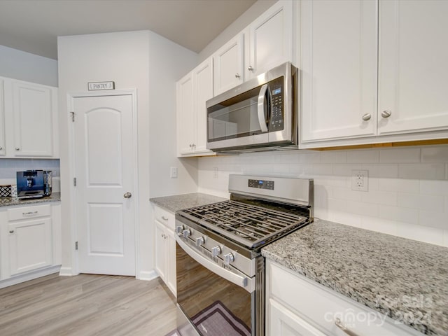 kitchen with stainless steel appliances, light stone counters, decorative backsplash, white cabinets, and light wood-type flooring