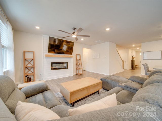 living room featuring ceiling fan, a large fireplace, and light hardwood / wood-style flooring