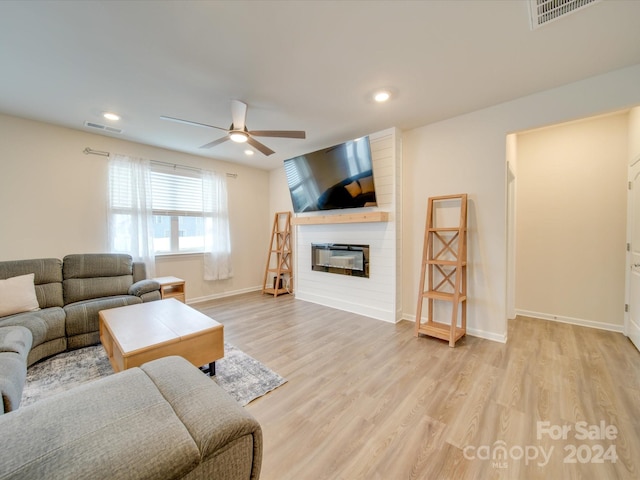 living room featuring ceiling fan, a large fireplace, and light hardwood / wood-style floors