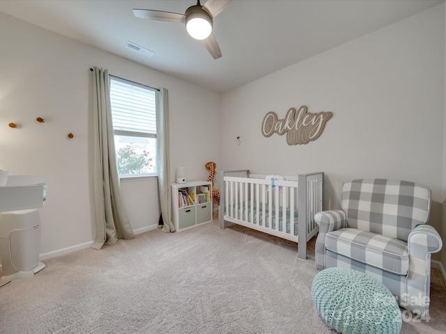 carpeted bedroom with ceiling fan and a crib