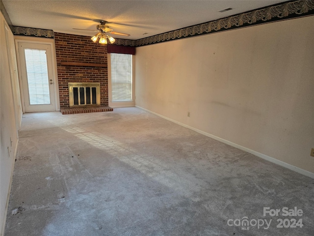 unfurnished living room with carpet, a textured ceiling, a brick fireplace, and ceiling fan