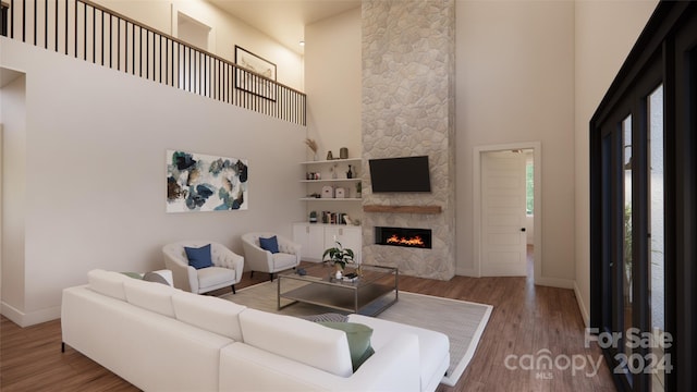 living room with hardwood / wood-style floors, a stone fireplace, and a towering ceiling