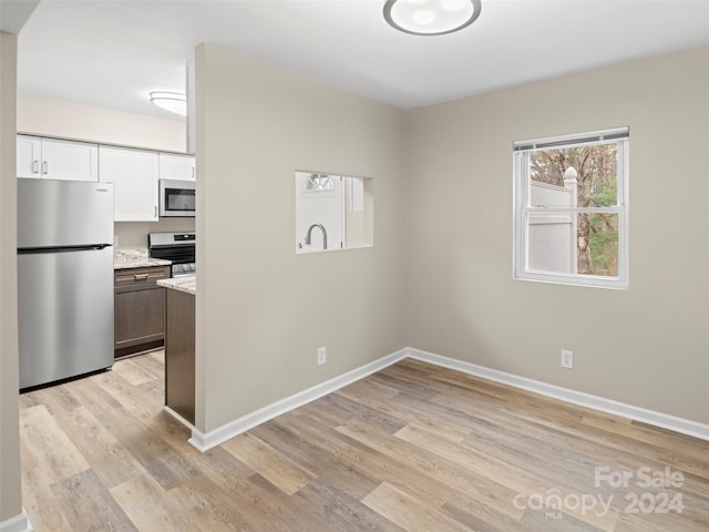 kitchen with white cabinets, appliances with stainless steel finishes, light hardwood / wood-style flooring, and light stone countertops