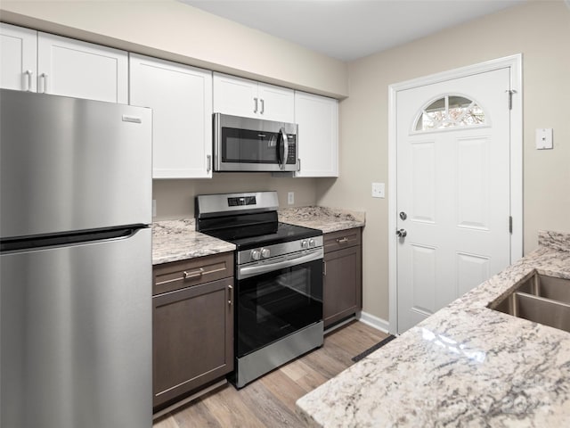 kitchen featuring white cabinets, light hardwood / wood-style flooring, light stone countertops, dark brown cabinetry, and stainless steel appliances