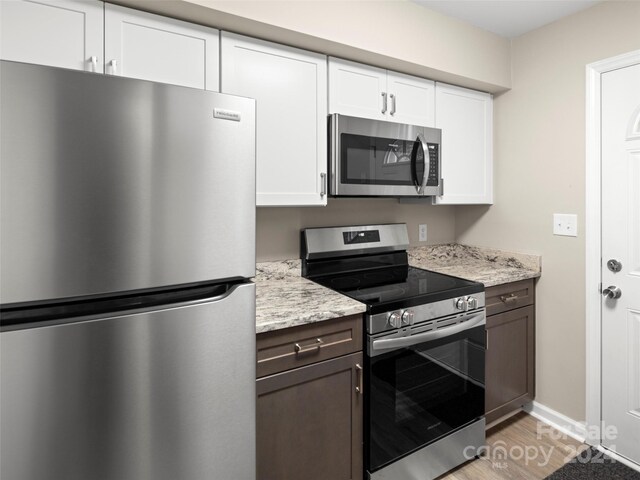 kitchen featuring dark brown cabinetry, white cabinetry, light stone countertops, light hardwood / wood-style floors, and appliances with stainless steel finishes