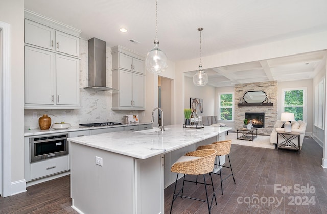 kitchen with dark hardwood / wood-style floors, wall chimney range hood, and an island with sink