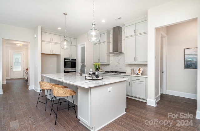 kitchen featuring appliances with stainless steel finishes, dark hardwood / wood-style flooring, a kitchen island with sink, and wall chimney range hood