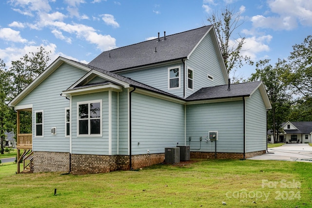 rear view of property with central AC unit and a lawn