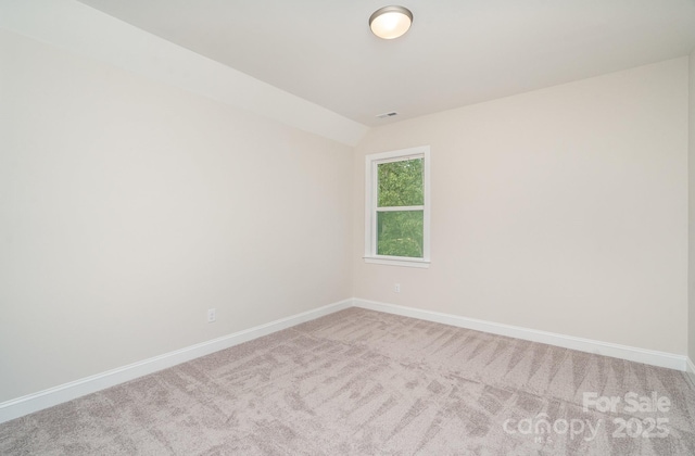 spare room featuring vaulted ceiling, carpet floors, visible vents, and baseboards