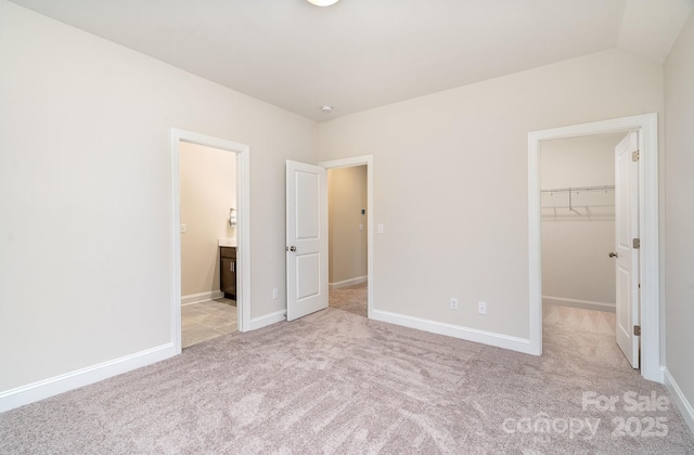 unfurnished bedroom with light carpet, baseboards, a walk in closet, and a closet