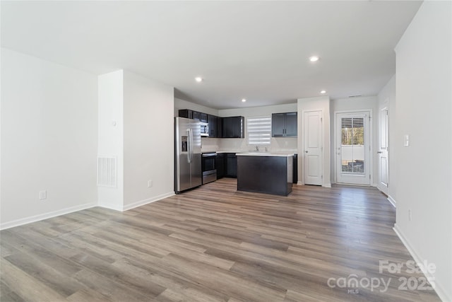 kitchen featuring sink, backsplash, appliances with stainless steel finishes, a kitchen island, and hardwood / wood-style flooring