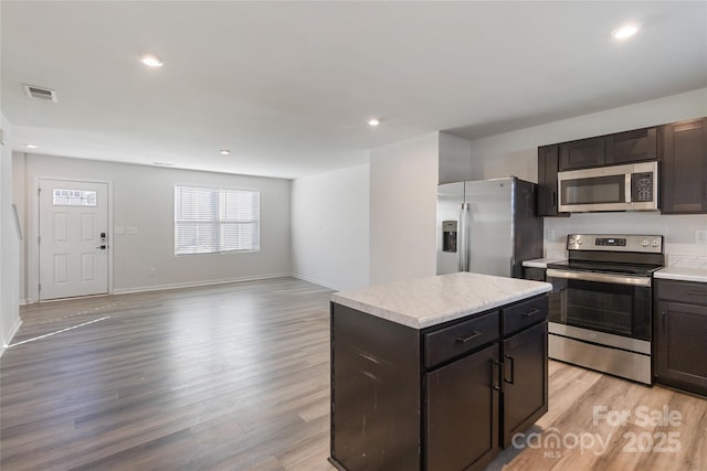 kitchen with light wood-type flooring, appliances with stainless steel finishes, a center island, and dark brown cabinets