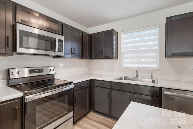 kitchen with appliances with stainless steel finishes, dark brown cabinetry, light hardwood / wood-style flooring, and sink