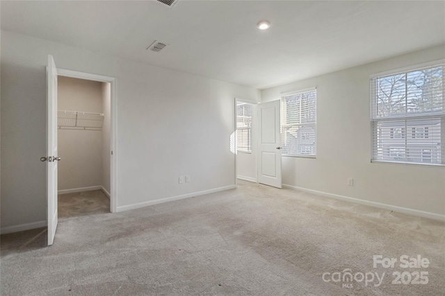 unfurnished bedroom with a closet, a walk in closet, light carpet, and multiple windows