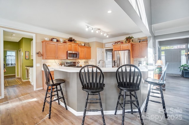 kitchen with light hardwood / wood-style floors, a kitchen bar, appliances with stainless steel finishes, and tasteful backsplash