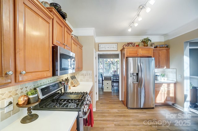 kitchen with decorative backsplash, light hardwood / wood-style floors, crown molding, and stainless steel appliances