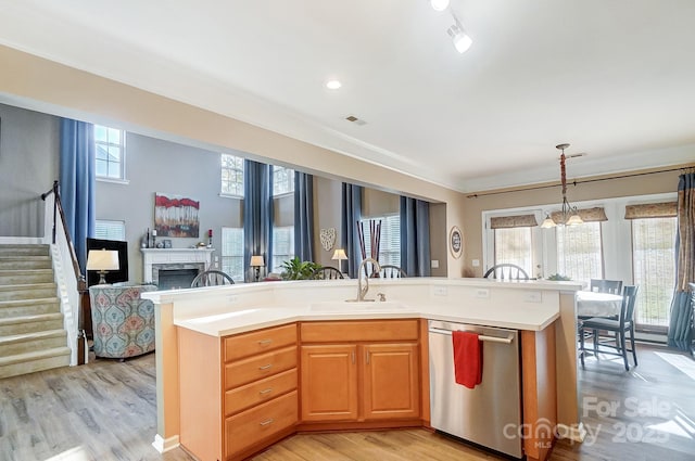 kitchen with dishwasher, sink, light hardwood / wood-style flooring, decorative light fixtures, and a kitchen island with sink