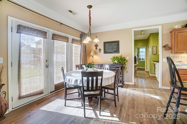 dining room with ornamental molding, a notable chandelier, and light wood-type flooring