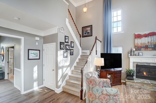 stairway featuring a stone fireplace, wood-type flooring, ornamental molding, and a towering ceiling