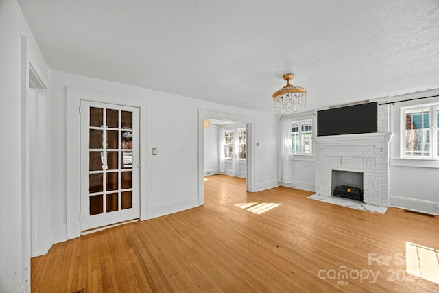 unfurnished living room with a brick fireplace, an inviting chandelier, a textured ceiling, and hardwood / wood-style flooring