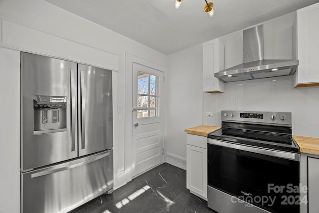 kitchen featuring wood counters, stainless steel appliances, white cabinetry, and wall chimney range hood