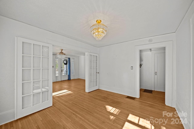 unfurnished room with hardwood / wood-style floors, a notable chandelier, a textured ceiling, and french doors