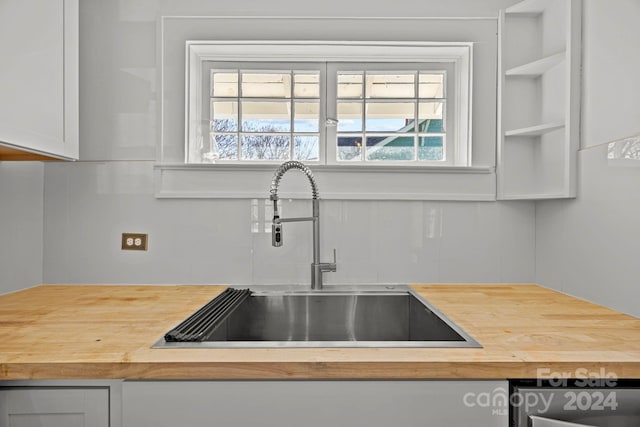 room details with butcher block countertops, white cabinetry, and sink