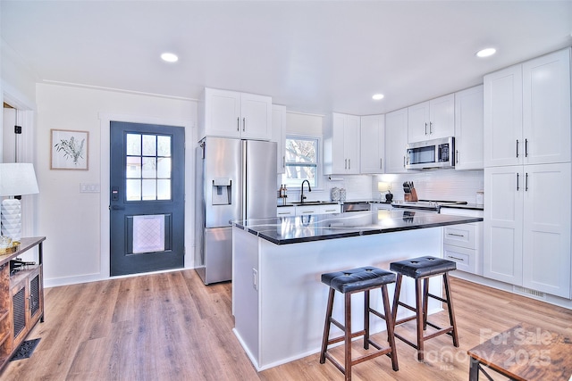 kitchen with a breakfast bar, white cabinets, sink, light hardwood / wood-style flooring, and appliances with stainless steel finishes