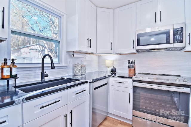 kitchen featuring white cabinetry, sink, stainless steel appliances, light hardwood / wood-style flooring, and backsplash