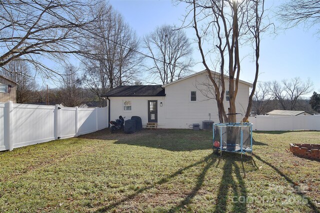 rear view of property featuring a lawn, a trampoline, and central AC