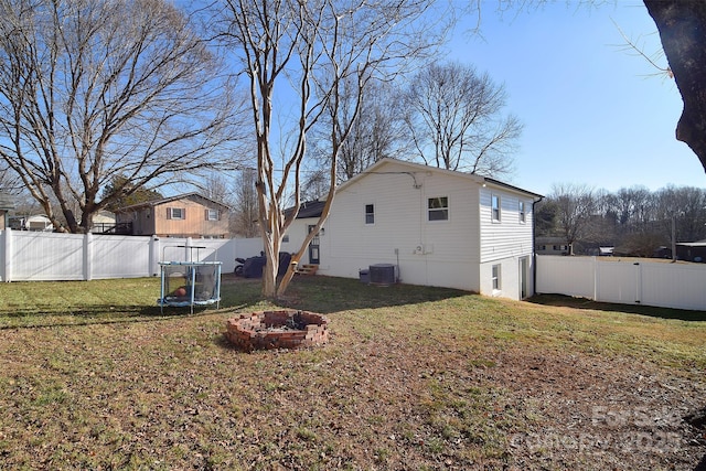 back of property featuring a lawn, an outdoor fire pit, central AC unit, and a trampoline