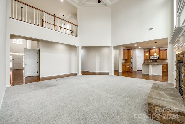 unfurnished living room featuring a stone fireplace, ornate columns, a high ceiling, and dark colored carpet