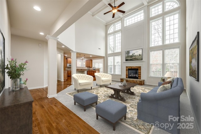 living room featuring a fireplace, decorative columns, a high ceiling, ceiling fan, and dark wood-type flooring