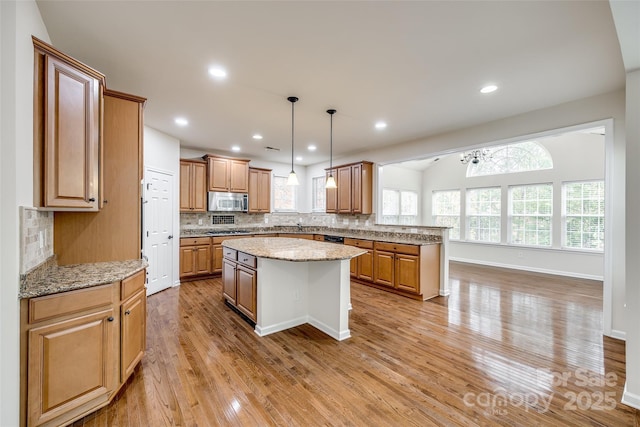 kitchen with a center island, stainless steel appliances, light stone countertops, light hardwood / wood-style floors, and backsplash