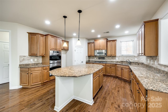 kitchen with a kitchen island, appliances with stainless steel finishes, dark wood-type flooring, and pendant lighting