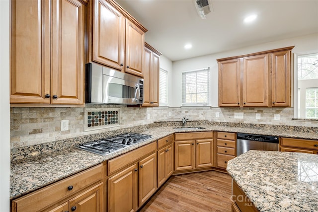 kitchen featuring sink, backsplash, light hardwood / wood-style floors, stainless steel appliances, and light stone countertops