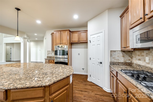 kitchen featuring pendant lighting, light stone countertops, stainless steel appliances, and a center island