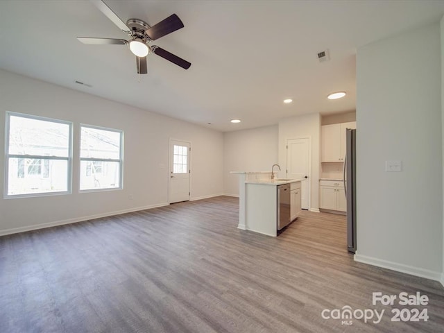 interior space with white cabinetry, ceiling fan, stainless steel appliances, a center island with sink, and light wood-type flooring